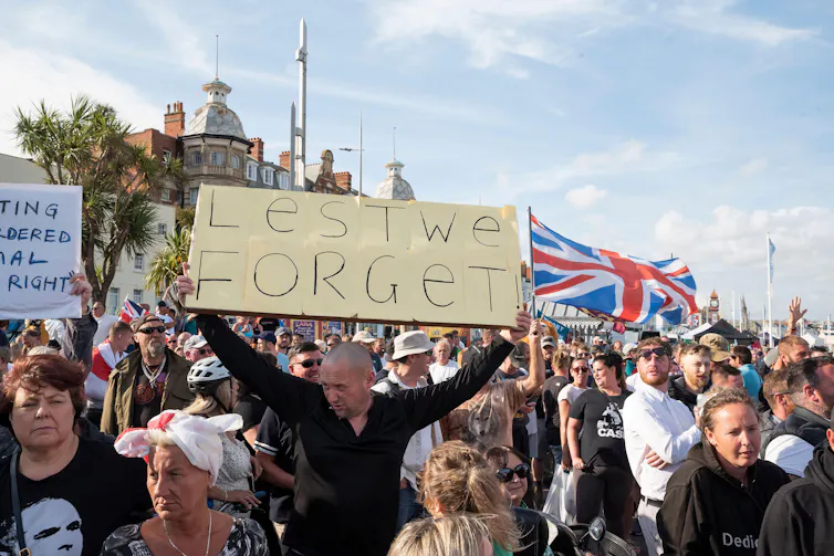 A man at a protest holding up a sign reading 'lest we forget'.