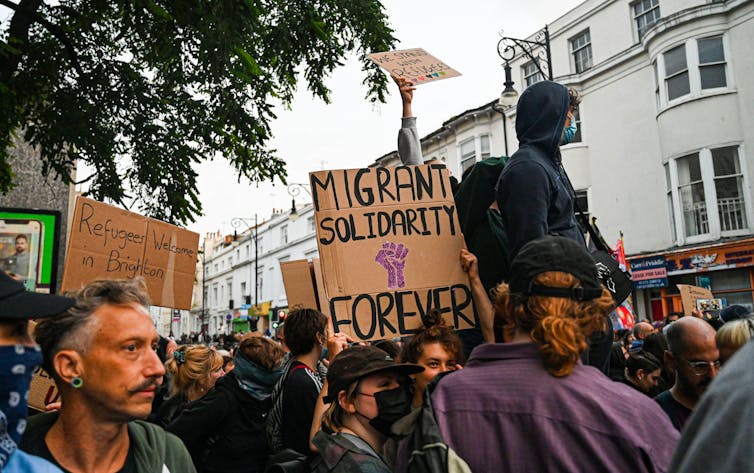 Protesters in Brighton with a cardboard sign reading 'migrant solidarity forever'