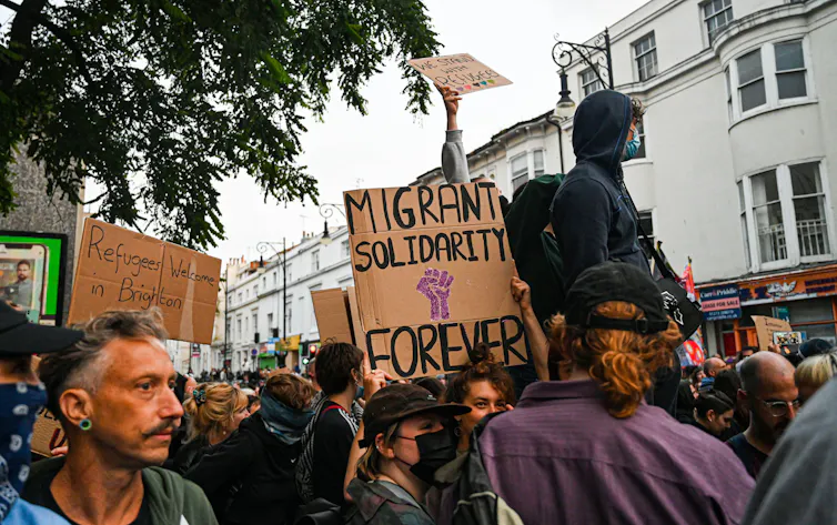 Protesters in Brighton with a cardboard sign reading 'migrant solidarity forever'
