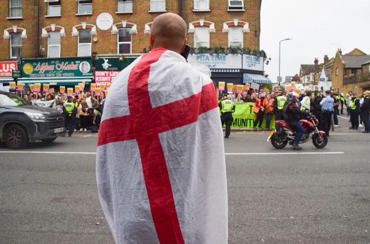 A lone right-wing protester draped in an England flag watches as crowds gather for a rally against the far-right