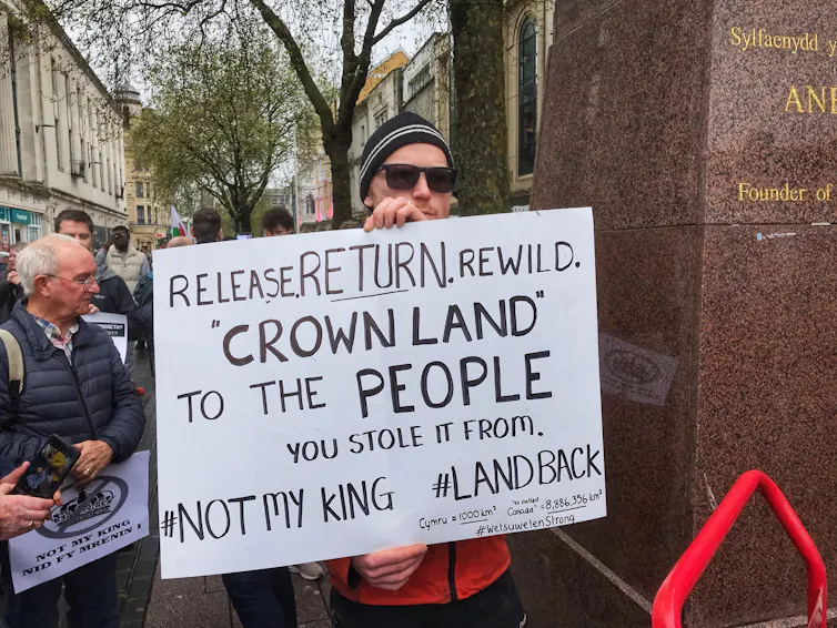 A man holding up a poster saying 'release return rewild crown land to the people you stole it from'.