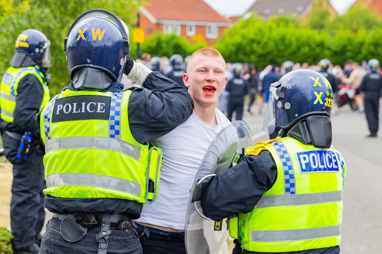 A man with a bloody mouth being apprehended by riot police.