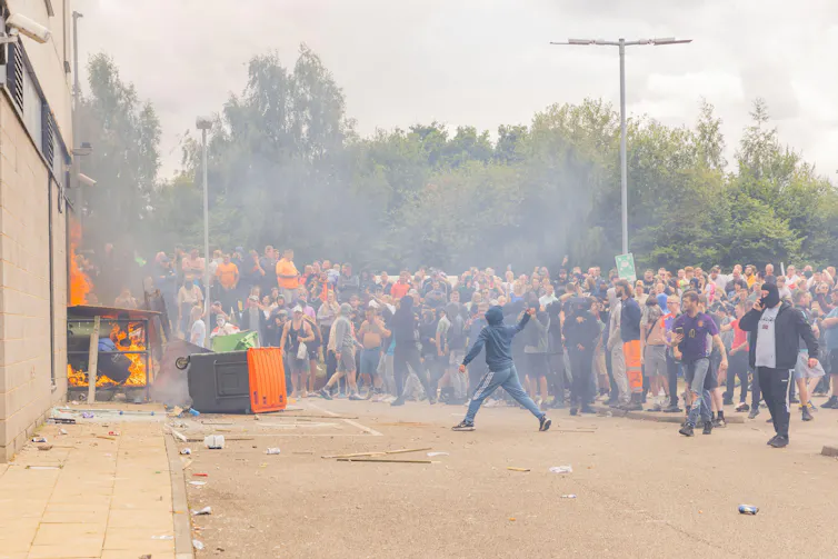A crowd of people outside a building that has been set on fire.