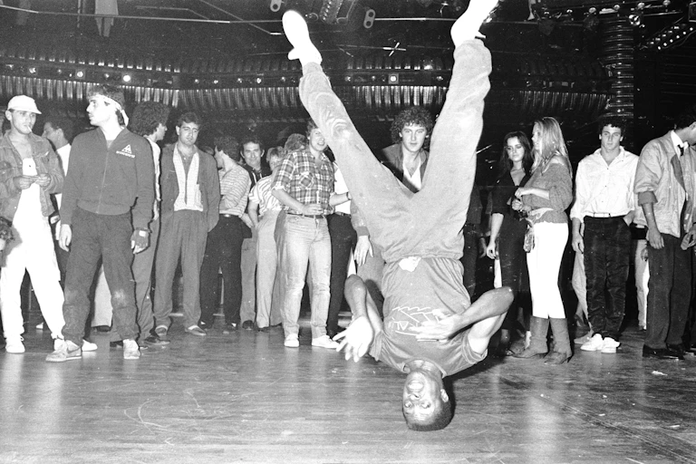 Black and white photo of young man performing a spin on his head at a dance club.