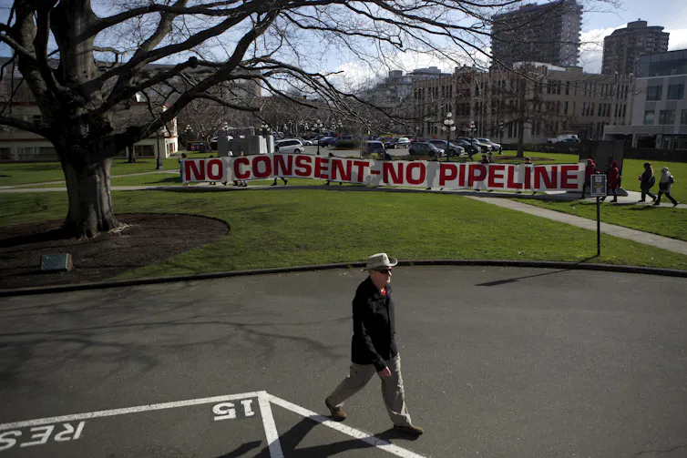 A sign on a lawn in front of buildings says no consent no pipeline.