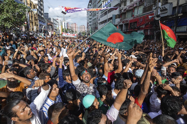 A large crowd of people, mostly men, wave the Bangladesh flag during a rally.