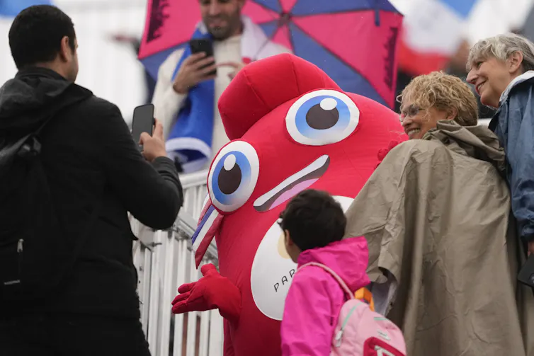 A mascot seen smiling at a child and adults surrounding it.