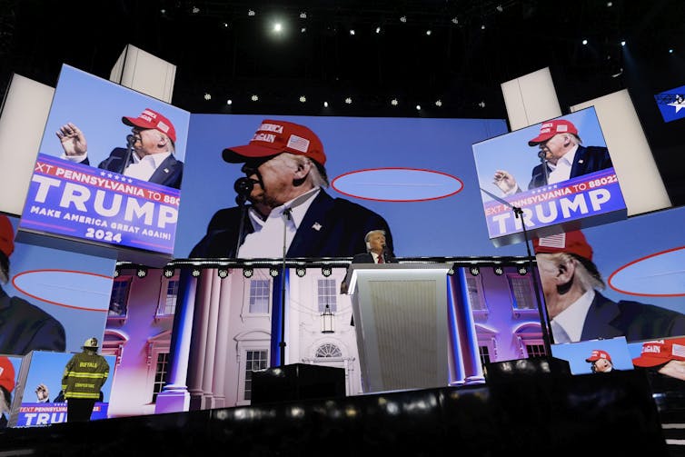 Screen projections of a man in a suit and red cap that reads 'make America great again.'