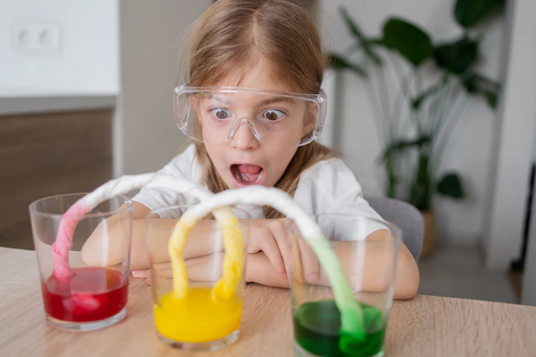 Young girl wearing protective eye wear looks at different colour dye in glasses
