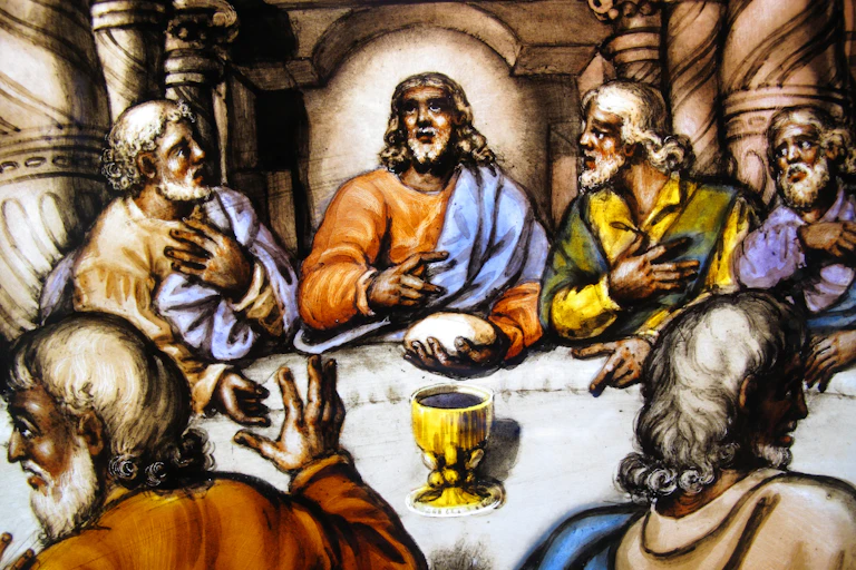 A painting showing several people at a table looking at a man in the center. On the table is a golden-color cup.
