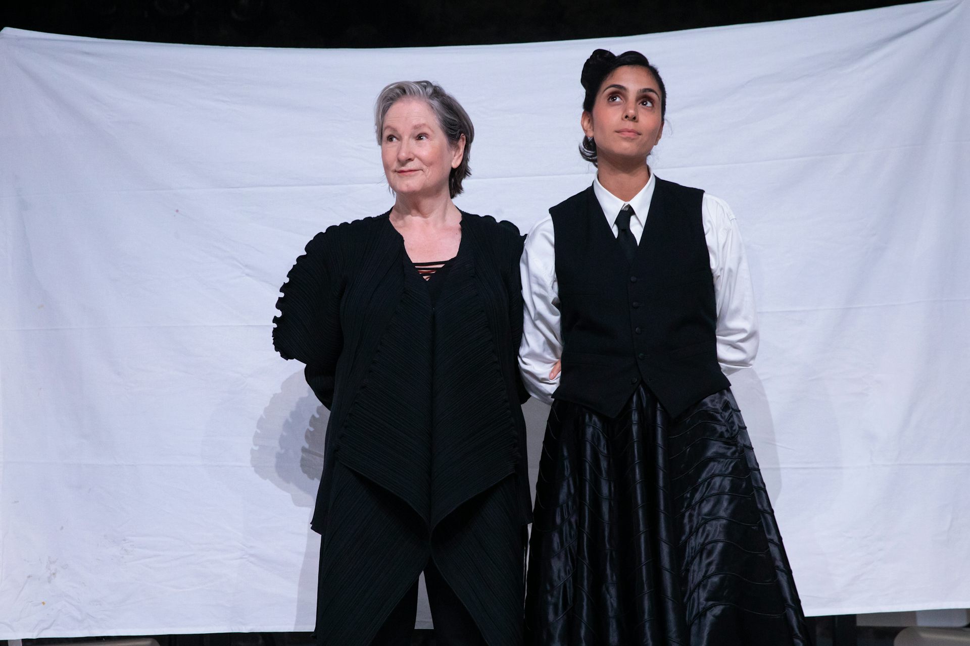 Two actresses stand in front of a white sheet