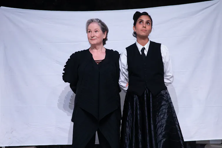 Two actresses stand in front of a white sheet