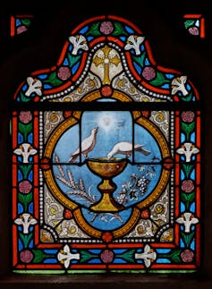 A painting with flower motifs around the edges while in the center is a goblet with two birds sitting on its edge.