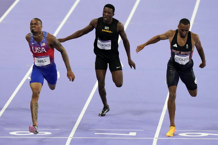 Three men, looking tired, running on tracks.