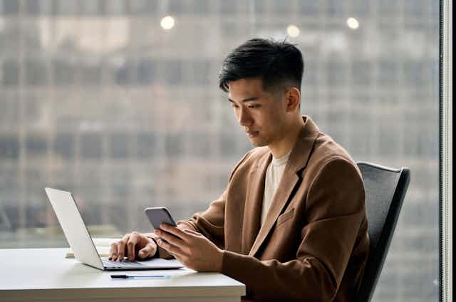 A man sits at a desk looking at his phone.