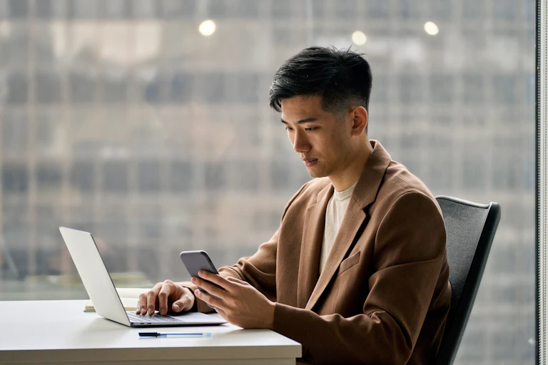 A man sits at a desk looking at his phone.