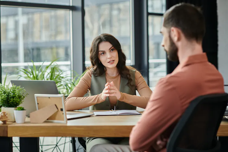 A woman speaks to a man, who has his back to the camera, in an office