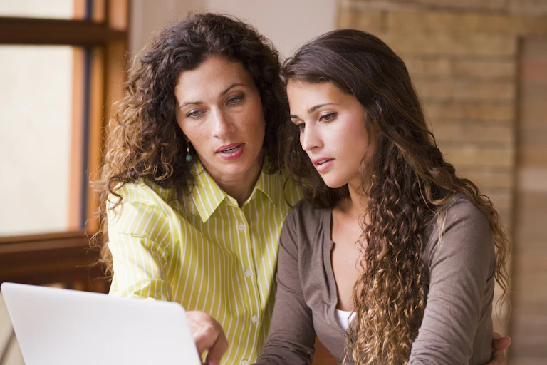 An older woman and a younger woman look at a screen on a laptop.