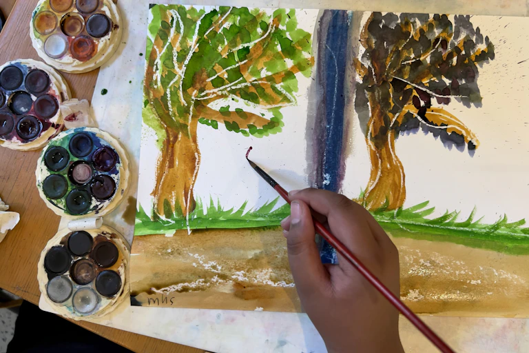 A hand paints trees in watercolours.