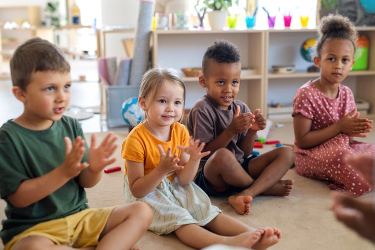 Four children in a child care centre sitting on the floor clapping.