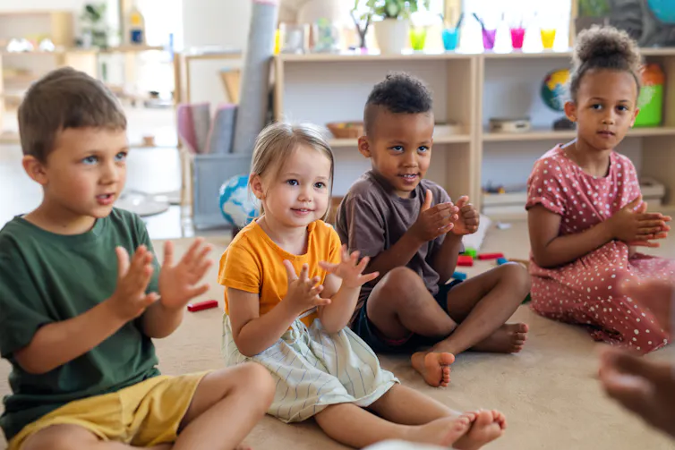 Four children in a child care centre sitting on the floor clapping.