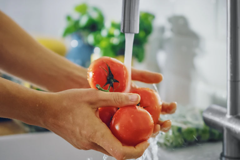 A person rinses tomatoes under a tap.