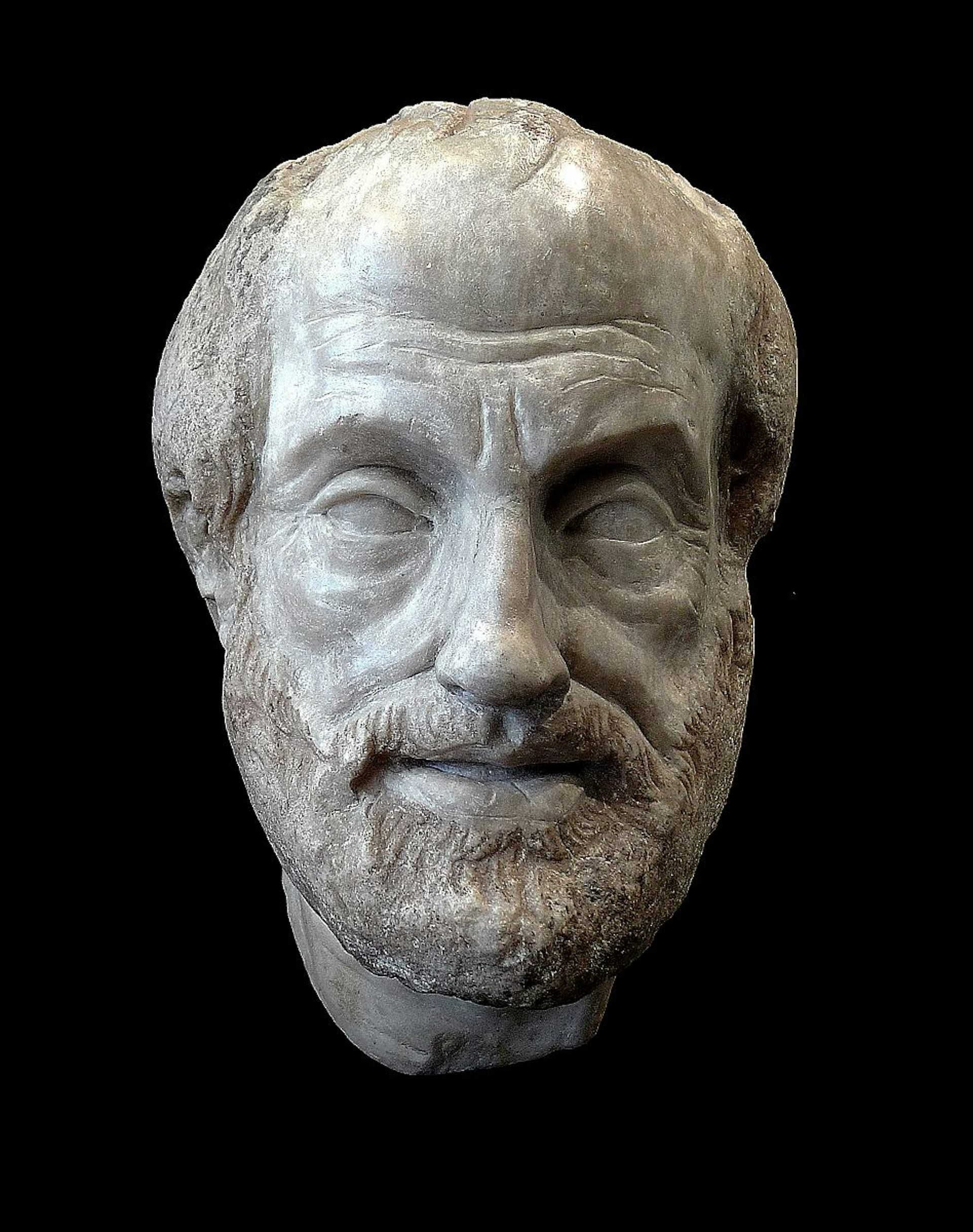 A stone bust of a balding man with a short beard on a black background.