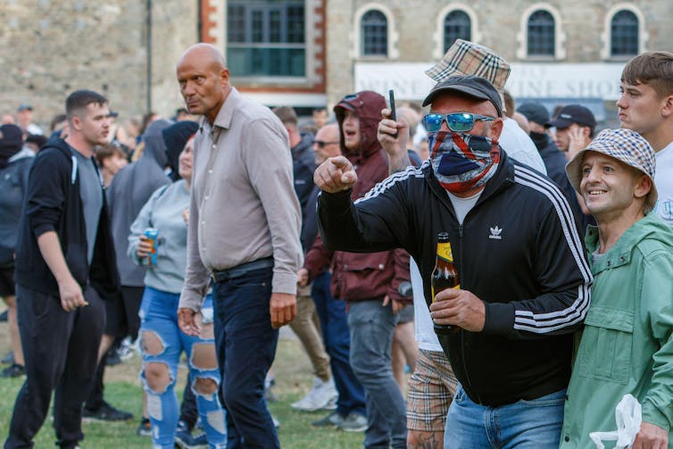 A group of men in a crowd, one with a union flag face covering.
