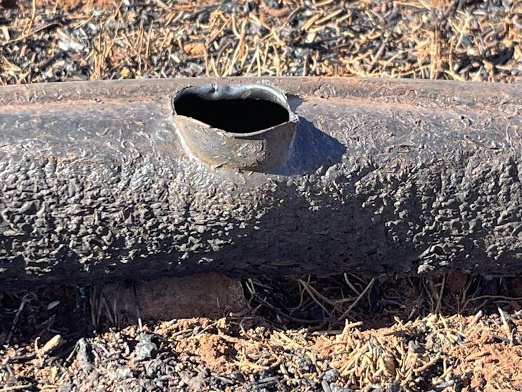A melted pipe with a hole in it lays on the ground.