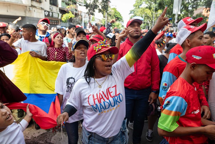 A woman at the front of a large crowd wearing a t-shirt with the names of Chavez and Maduro on the front.