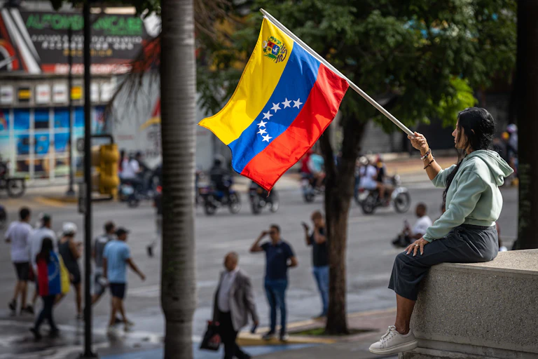 A woman sat holding a Venezuelan flag above a street.