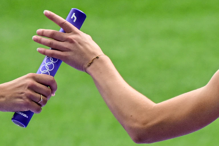 An athlete passes the baton in the women's 4x400m relay heat of the athletics event at the Paris 2024 Olympic Games.