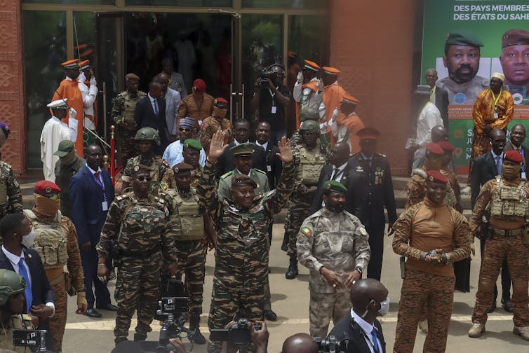 A group of men in army fatigues stand outside a building.