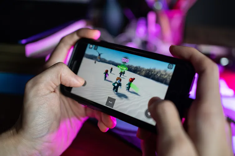 Close-up of hands holding a smartphone horizontally playing a 3D game with figures standing on a beach.
