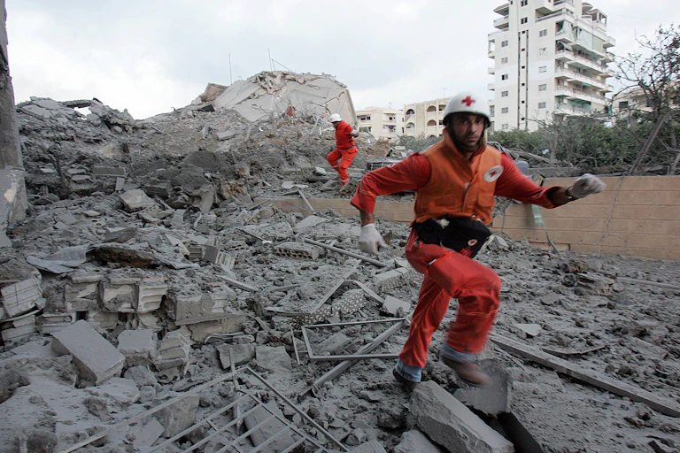 Workers in Red Cross uniform walk across rubble