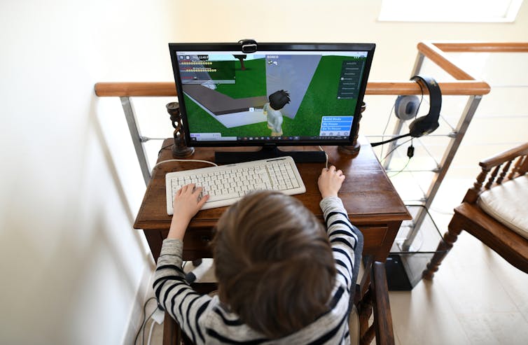 A wide view of a young child sitting at a PC playing a 3D online game.