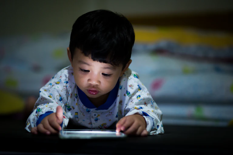 A young child in pyjamas playing on a tablet in a dark room.