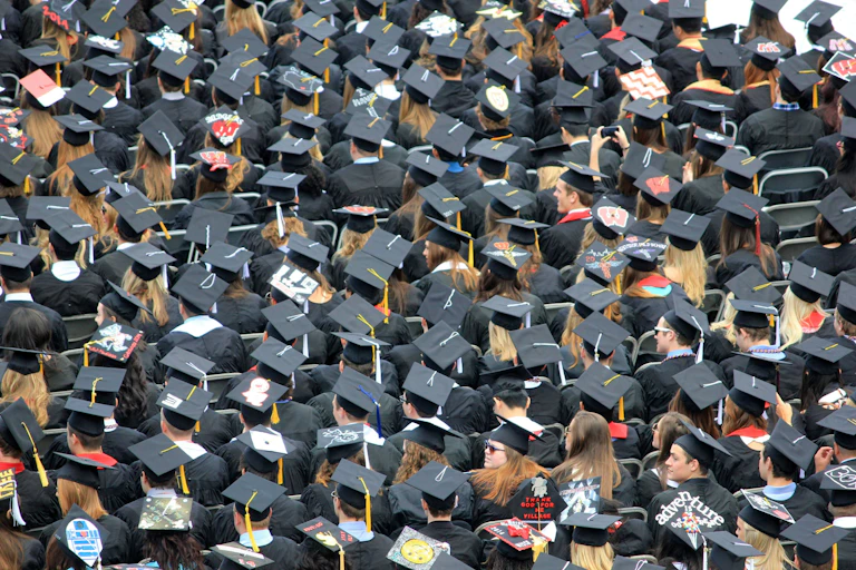 An aerial view of graduates in gowns and caps. Some graduates have messages and pictures on their caps.