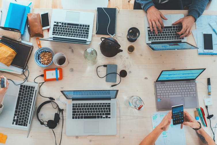 A large table with many laptops, drinks and people working.