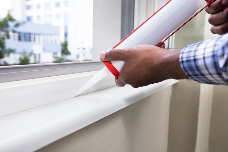 man uses sealant on window