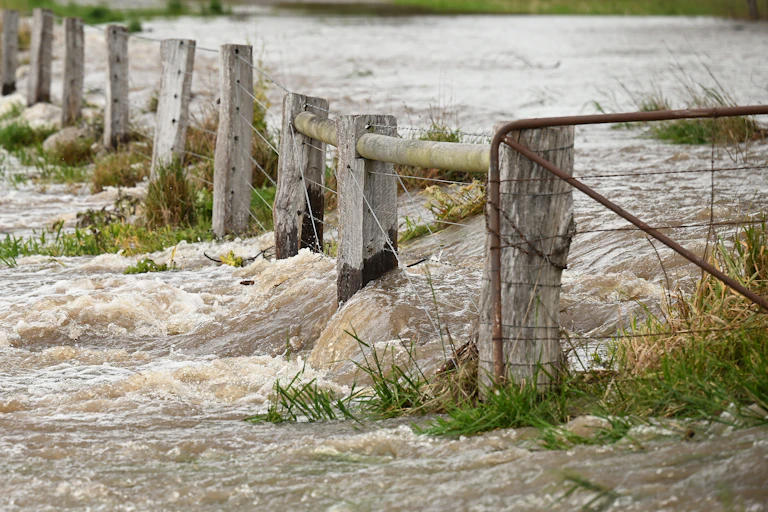 Floodwaters rush through a farm fence in rural Australia