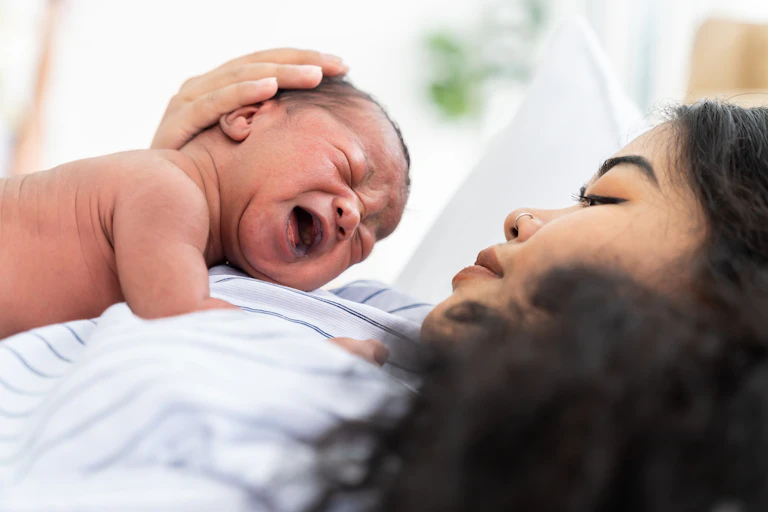 A newborn cries on her mother's chest.
