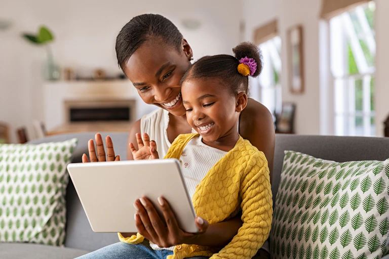 A smiling mum and daughter wave at the digital tablet the mother is holding