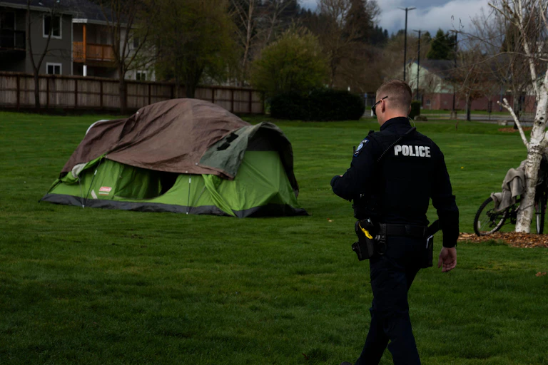 A police officer walking towards a large green camping tent in a public park