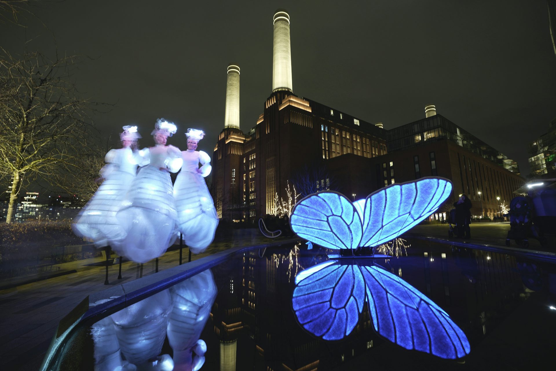 A blue illuminated butterfly art installation in front of an art deco decommissioned power plant at night time.