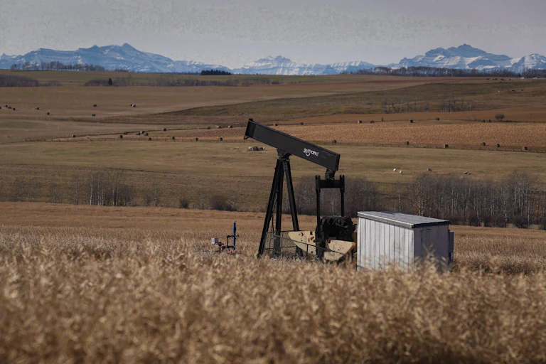 An old pumpjack in a farmer's field, with mountains in the background.