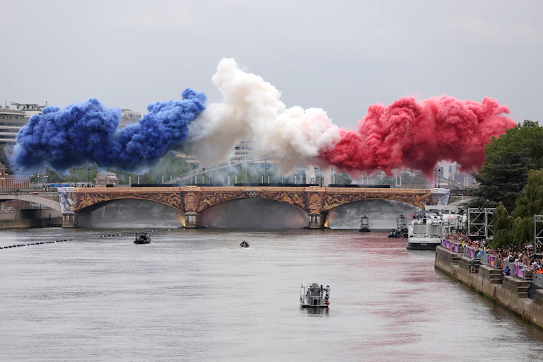 Huge billows of blue, white and red smoke rise above a bridge over a river.