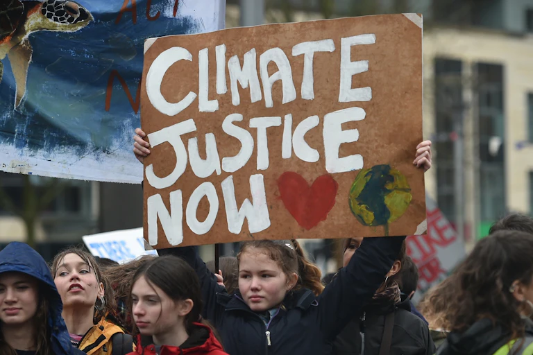 A girl holds up a sign that reads: Climate Justice Now