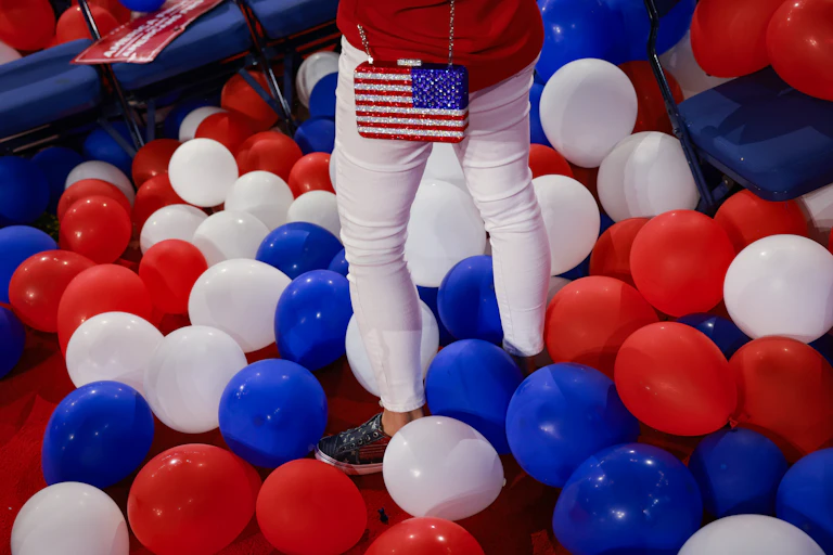 A person's legs standing among red, white and blue balloons on the floor.