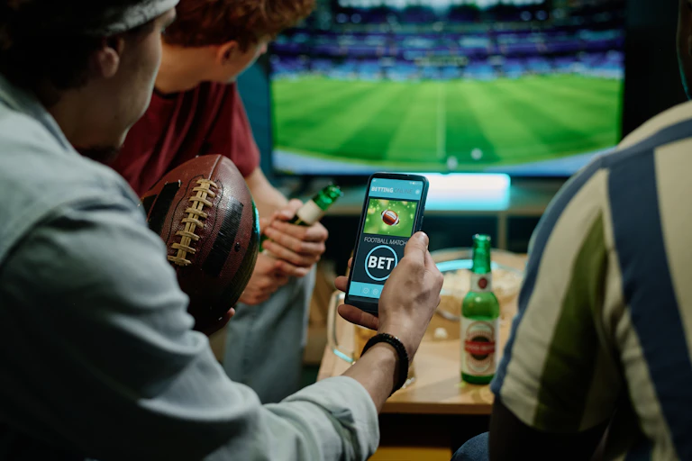 A group of young men watch a sports game and bet on a smartphone